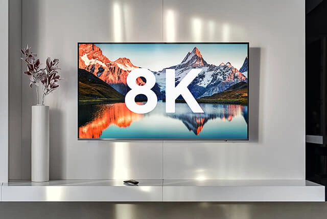 Телевизор на стене отображает изображение в формате 8K на фоне гор и озера