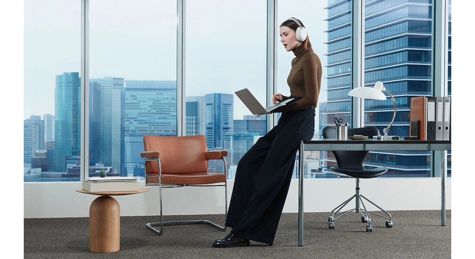 Женщина в белых наушниках Sony 1000X THE COLLEXION работает с ноутбуком в офисе