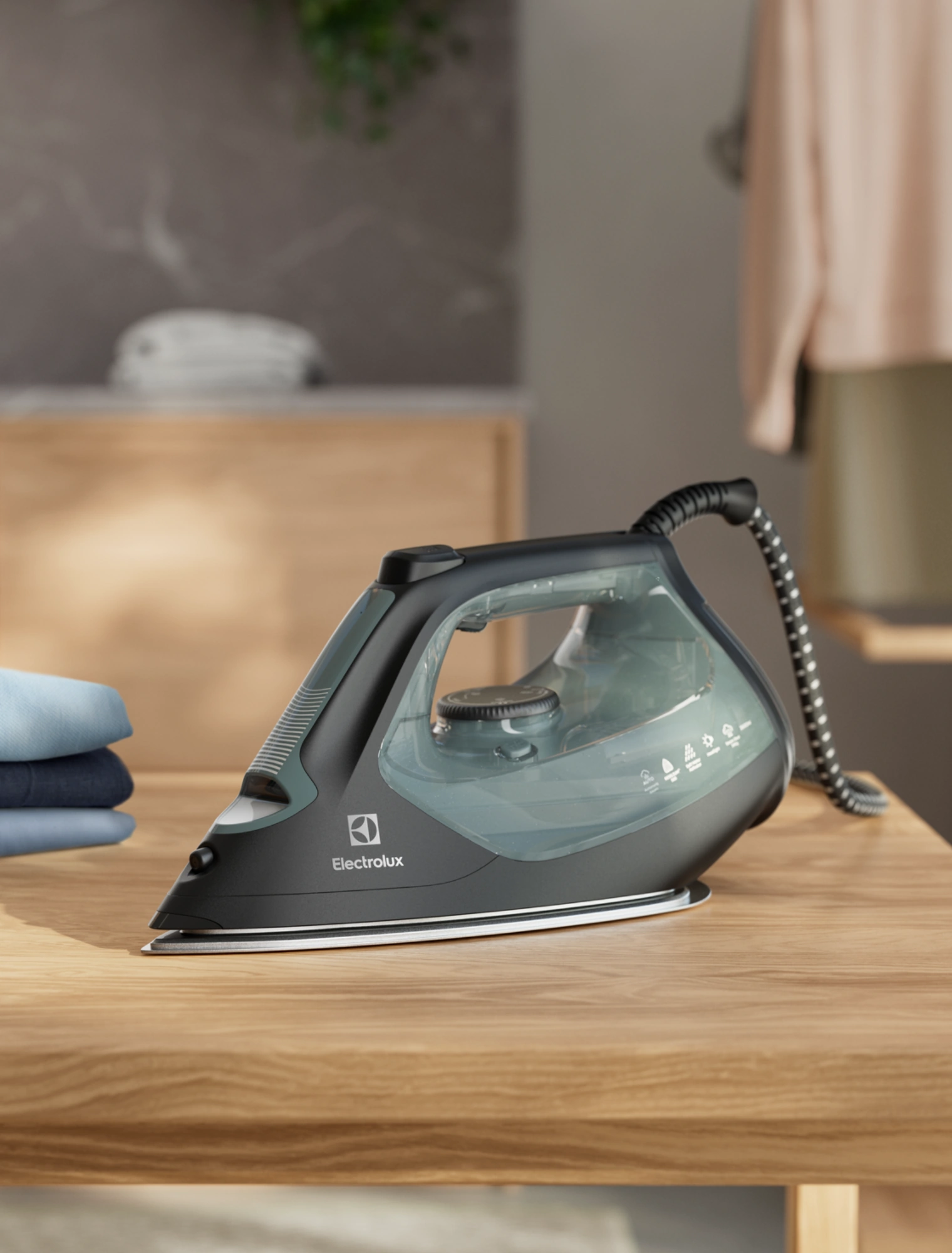 Утюг Electrolux E7SI2-6OG на деревянном столе рядом со стопкой выглаженного белья