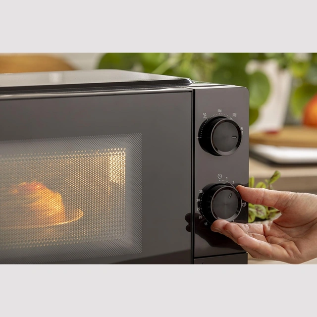 Рука устанавливает таймер чёрной микроволновой печи Gorenje