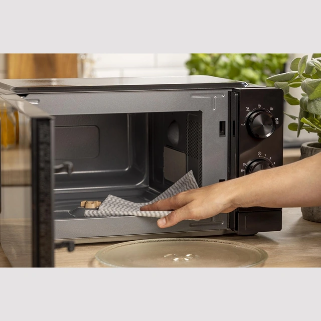 Руки протирают салфеткой лакированную камеру чёрной микроволновой печи Gorenje