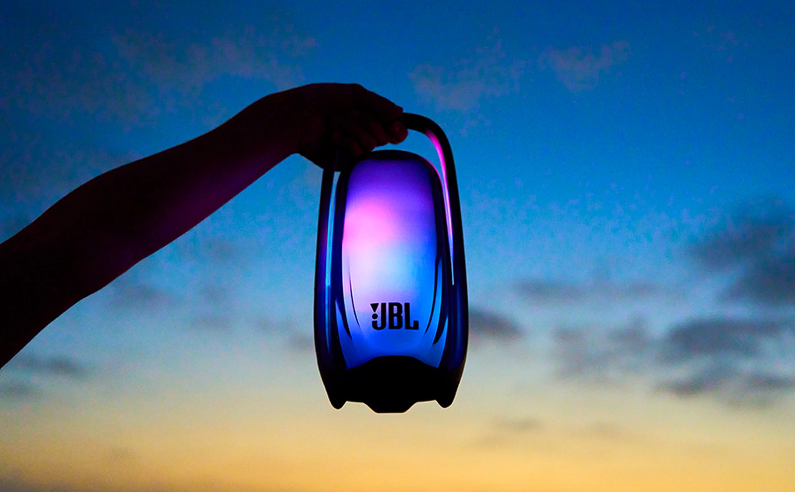 Колонка JBL Pulse 6 в руке на фоне вечернего неба